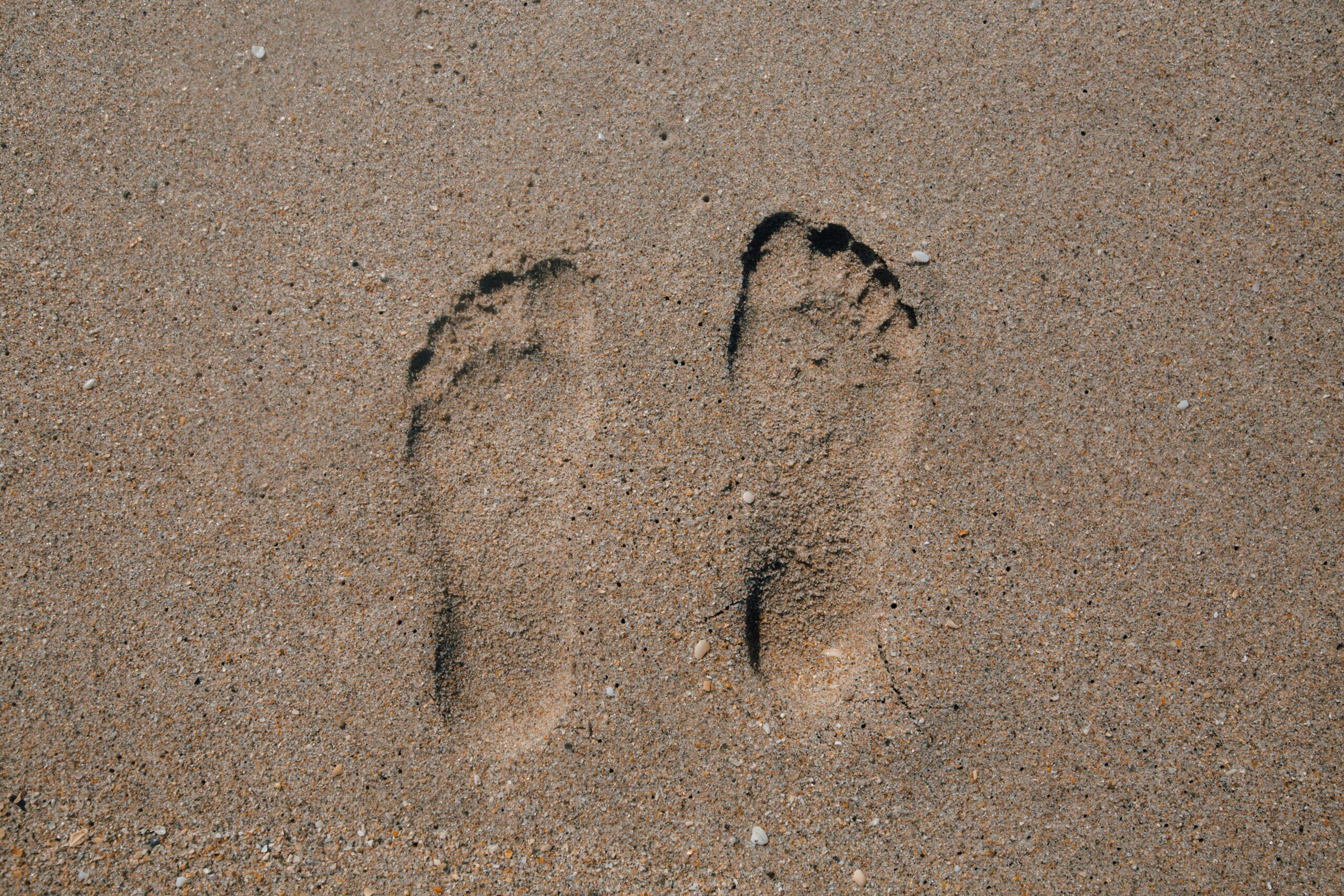 Close-up of two footprints in sand, evoking summer beach vibes.
